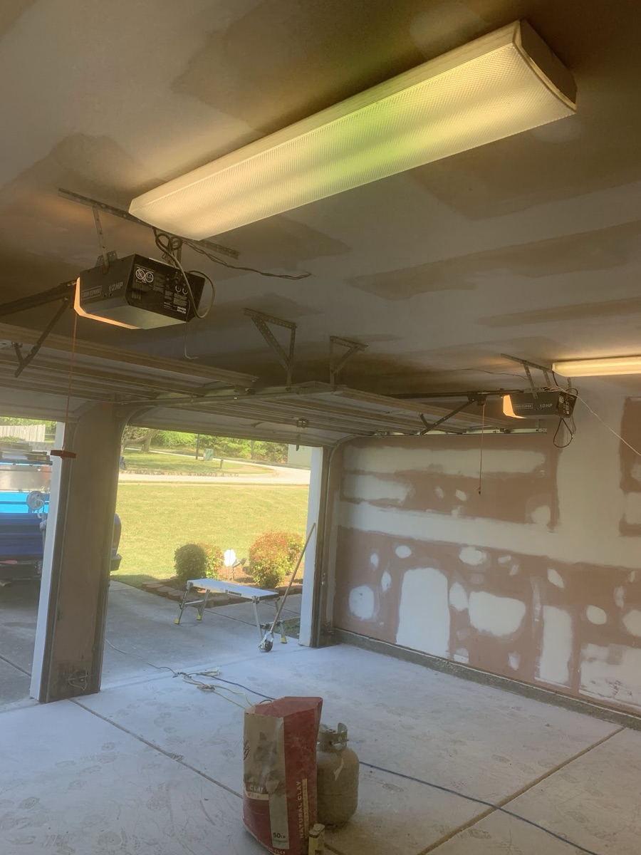 Garage with drywall finishing, light fixture, and door openers installed